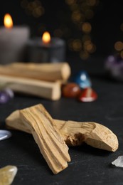 Photo of Palo santo sticks, gemstones and burning candles on black table against blurred lights, closeup