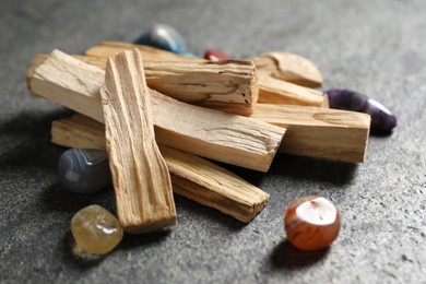 Photo of Palo santo sticks and gemstones on grey table, closeup