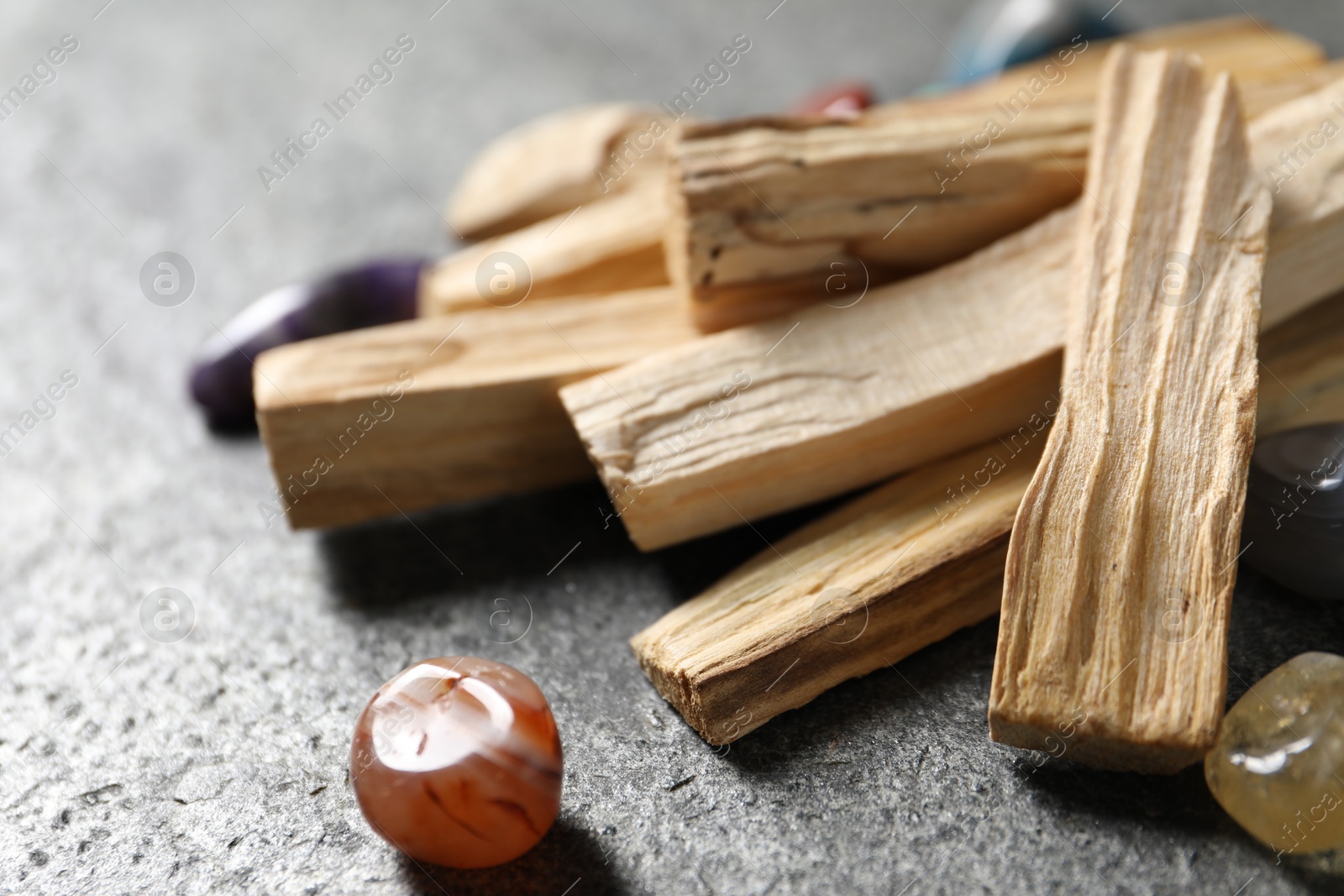 Photo of Palo santo sticks and gemstones on grey table, closeup