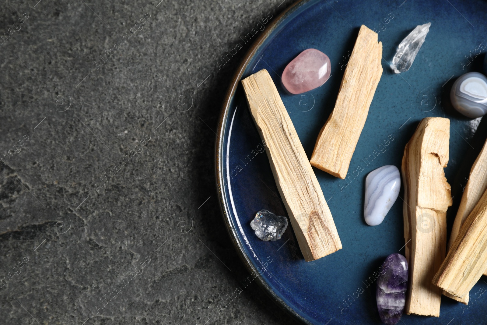 Photo of Palo santo sticks and gemstones on grey table, top view. Space for text