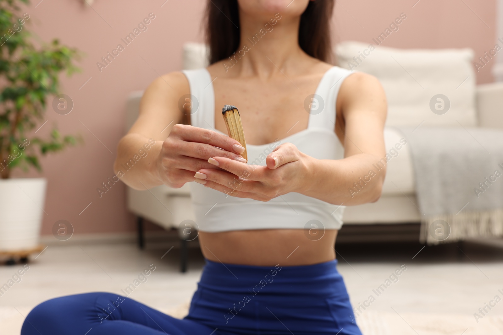 Photo of Woman with burnt palo santo stick on floor at home, closeup