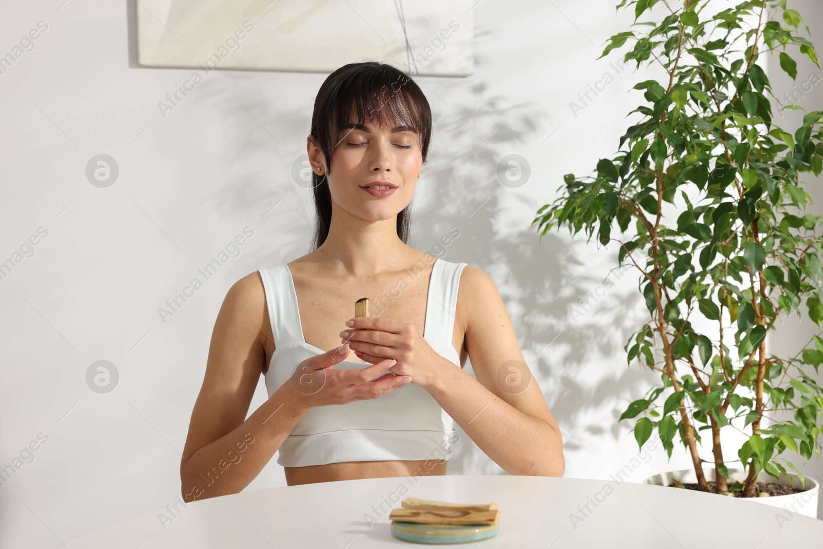 Photo of Woman with burnt palo santo stick at white table indoors