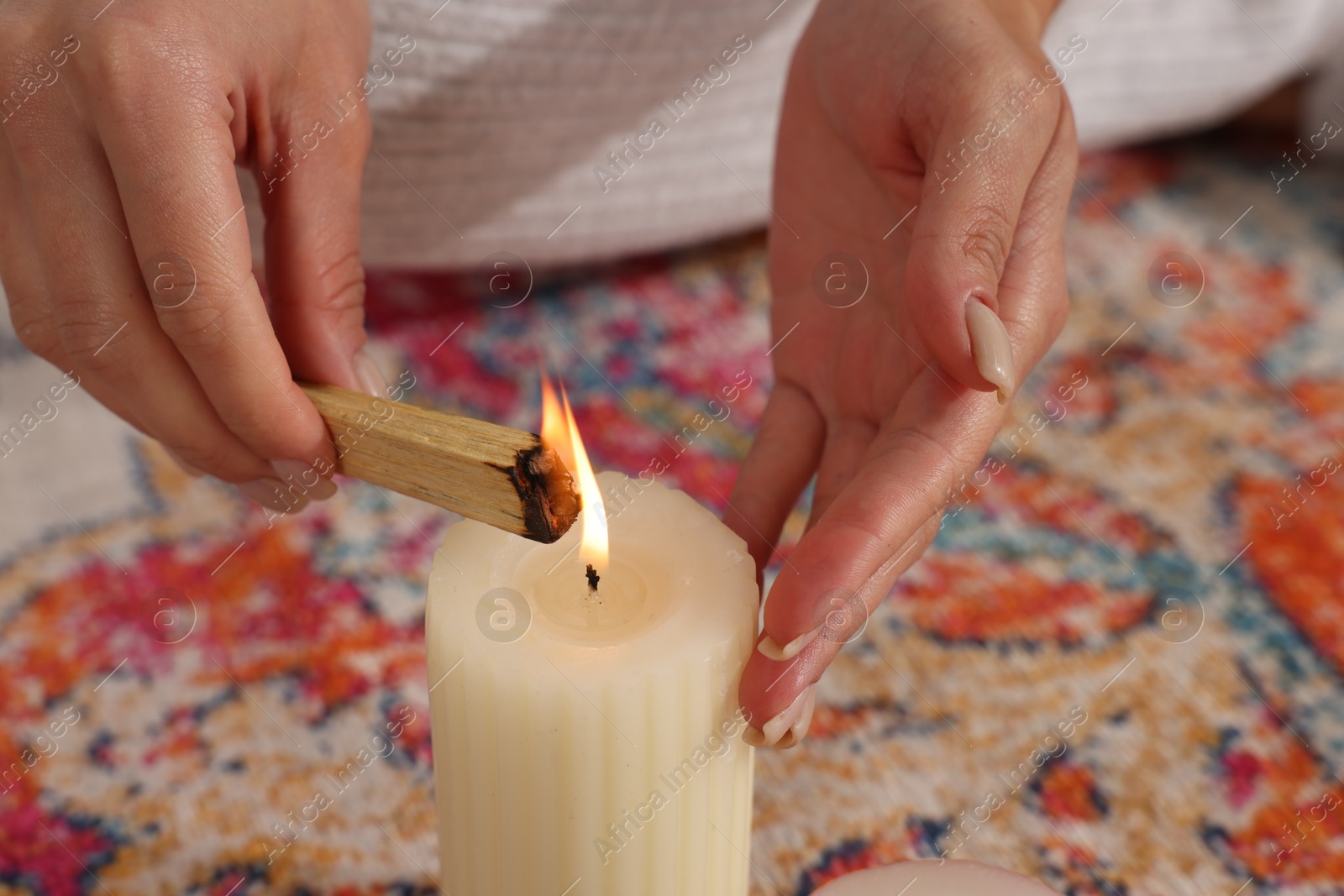 Photo of Woman lighting palo santo stick on floor at home, closeup