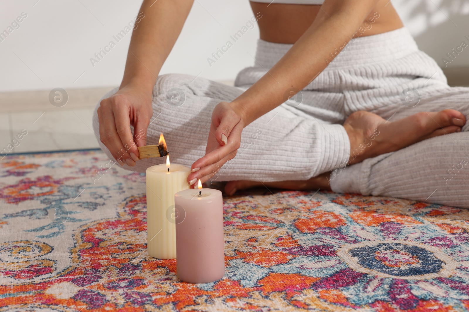 Photo of Woman lighting palo santo stick on floor at home, closeup