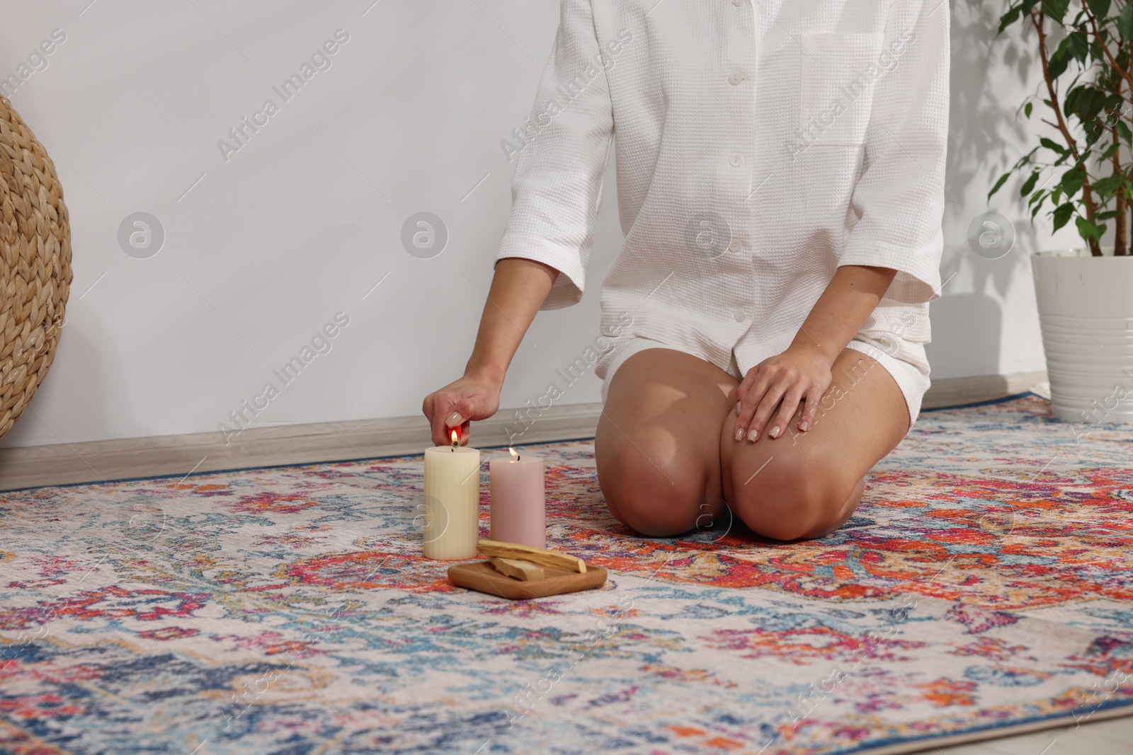 Photo of Woman lighting candle near palo santo sticks on floor at home, closeup. Space for text