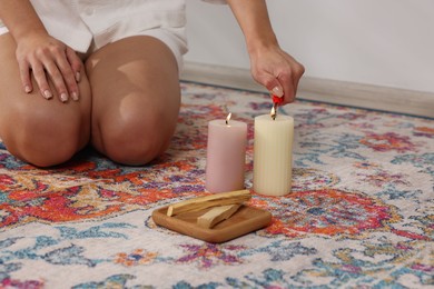 Photo of Woman lighting candle near palo santo sticks on floor at home, closeup. Space for text