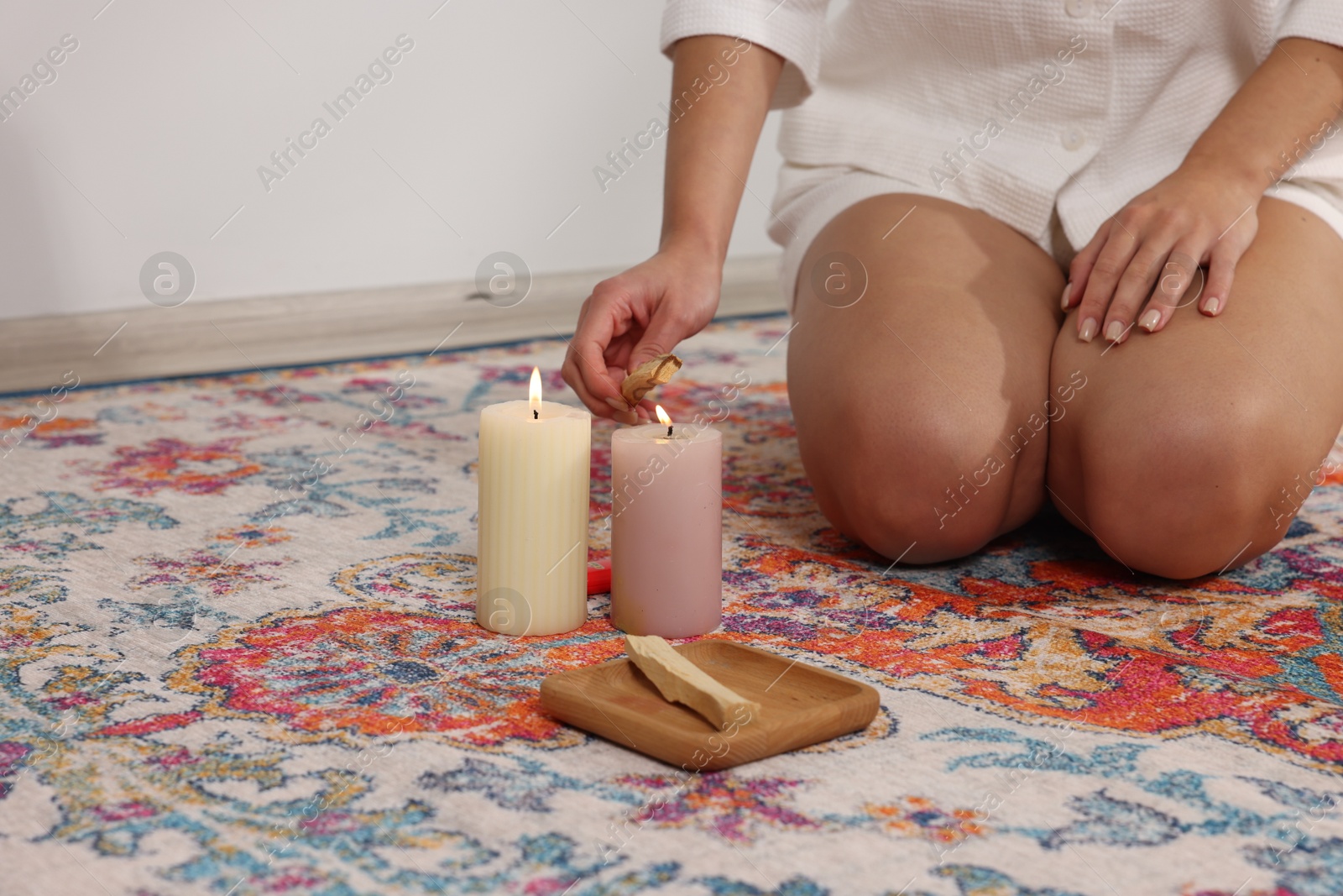 Photo of Woman lighting palo santo stick on floor at home, closeup. Space for text