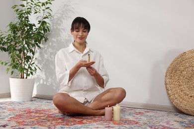 Woman with smoldering palo santo stick on floor at home, space for text