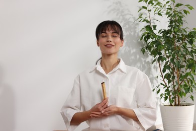 Woman with burning palo santo stick at home, space for text