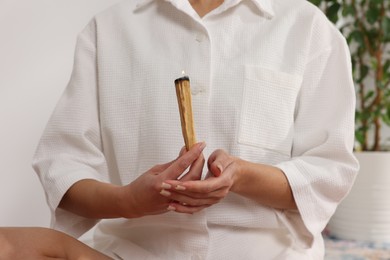 Photo of Woman with burning palo santo stick at home, closeup