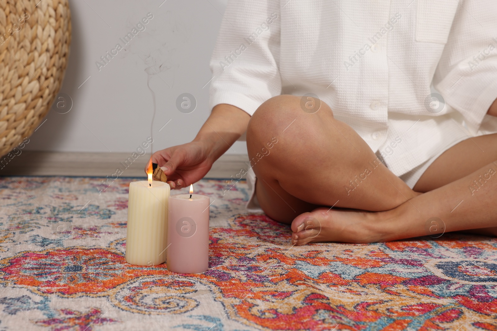 Photo of Woman lighting palo santo stick on floor at home, closeup