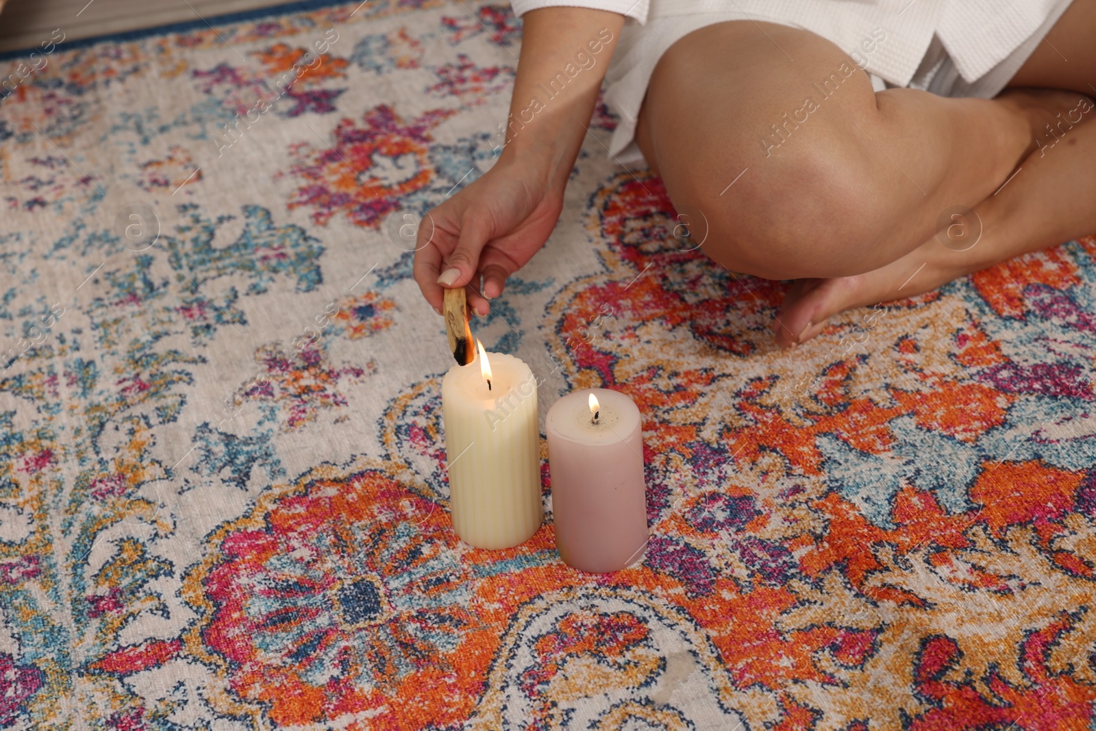 Photo of Woman lighting palo santo stick on floor at home, closeup