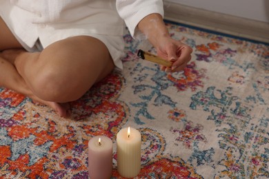 Photo of Woman with smoldering palo santo stick on floor at home, closeup