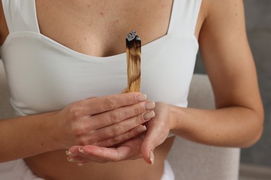 Photo of Woman with burnt palo santo stick at home, closeup