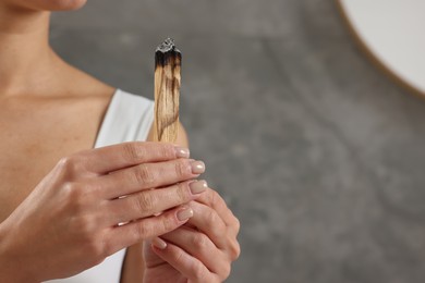 Photo of Woman with burnt palo santo stick at home, closeup. Space for text