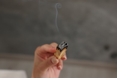 Photo of Woman with smoldering palo santo stick indoors, closeup