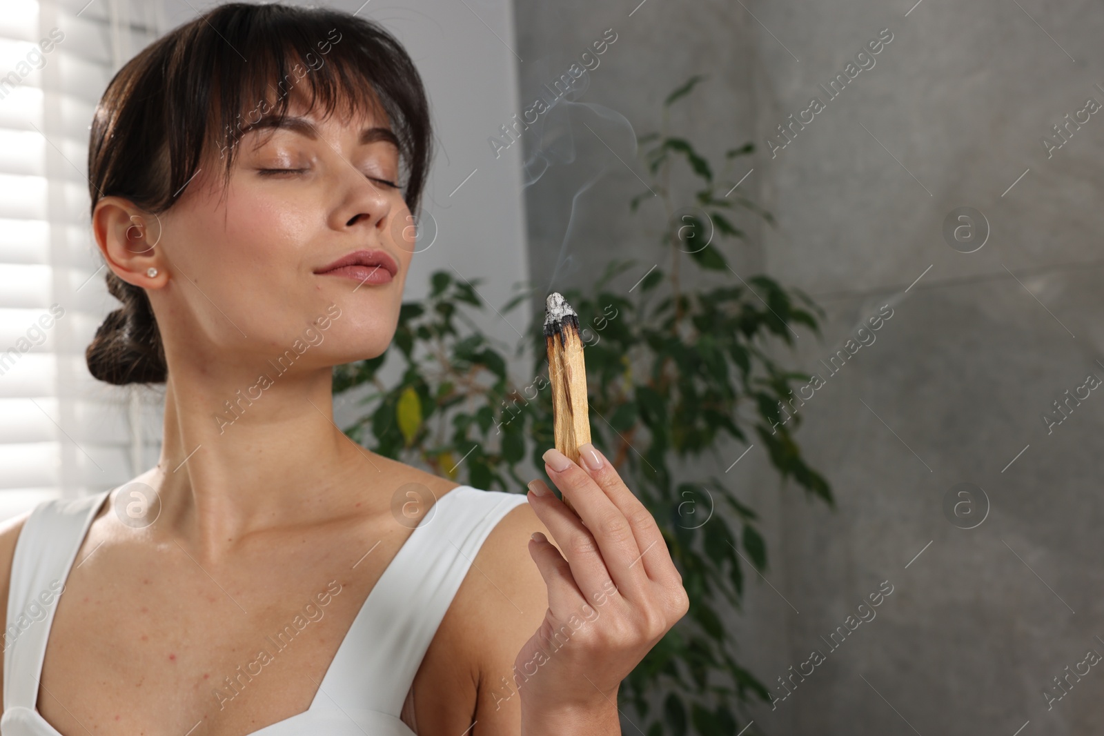 Photo of Woman with smoldering palo santo stick at home, space for text