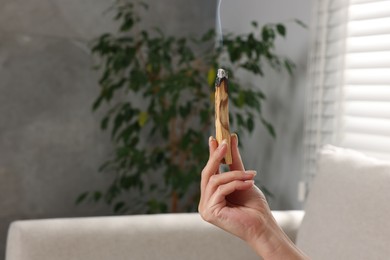 Photo of Woman with smoldering palo santo stick at home, closeup. Space for text