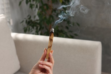 Photo of Woman with smoldering palo santo stick at home, closeup