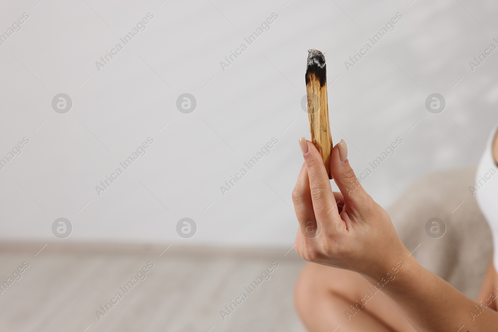 Photo of Woman with burnt palo santo stick at home, closeup. Space for text