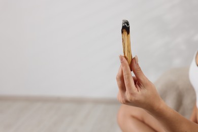 Photo of Woman with burnt palo santo stick at home, closeup. Space for text