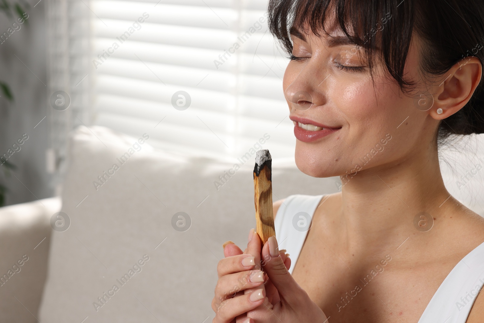 Photo of Woman with smoldering palo santo stick at home, space for text