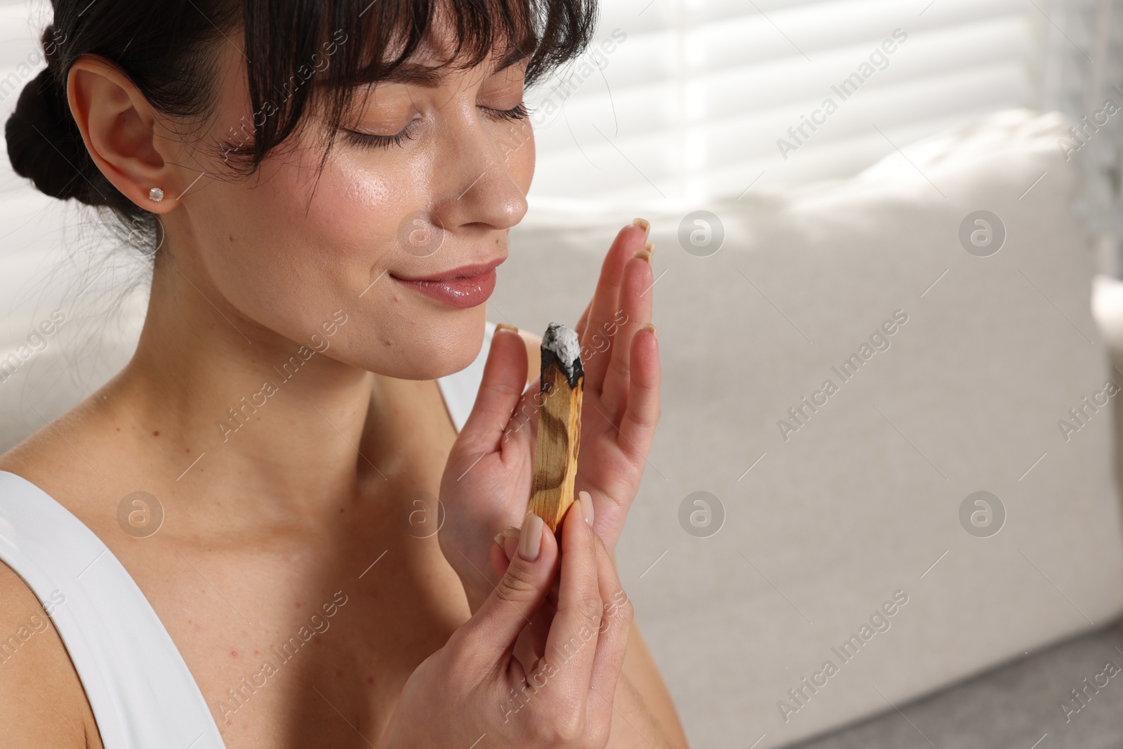 Photo of Woman with smoldering palo santo stick at home, space for text