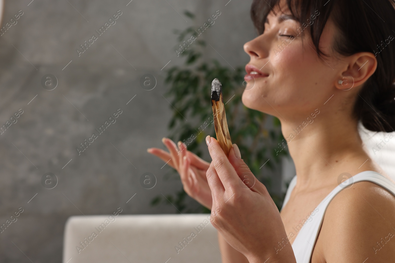 Photo of Woman with smoldering palo santo stick at home, selective focus. Space for text