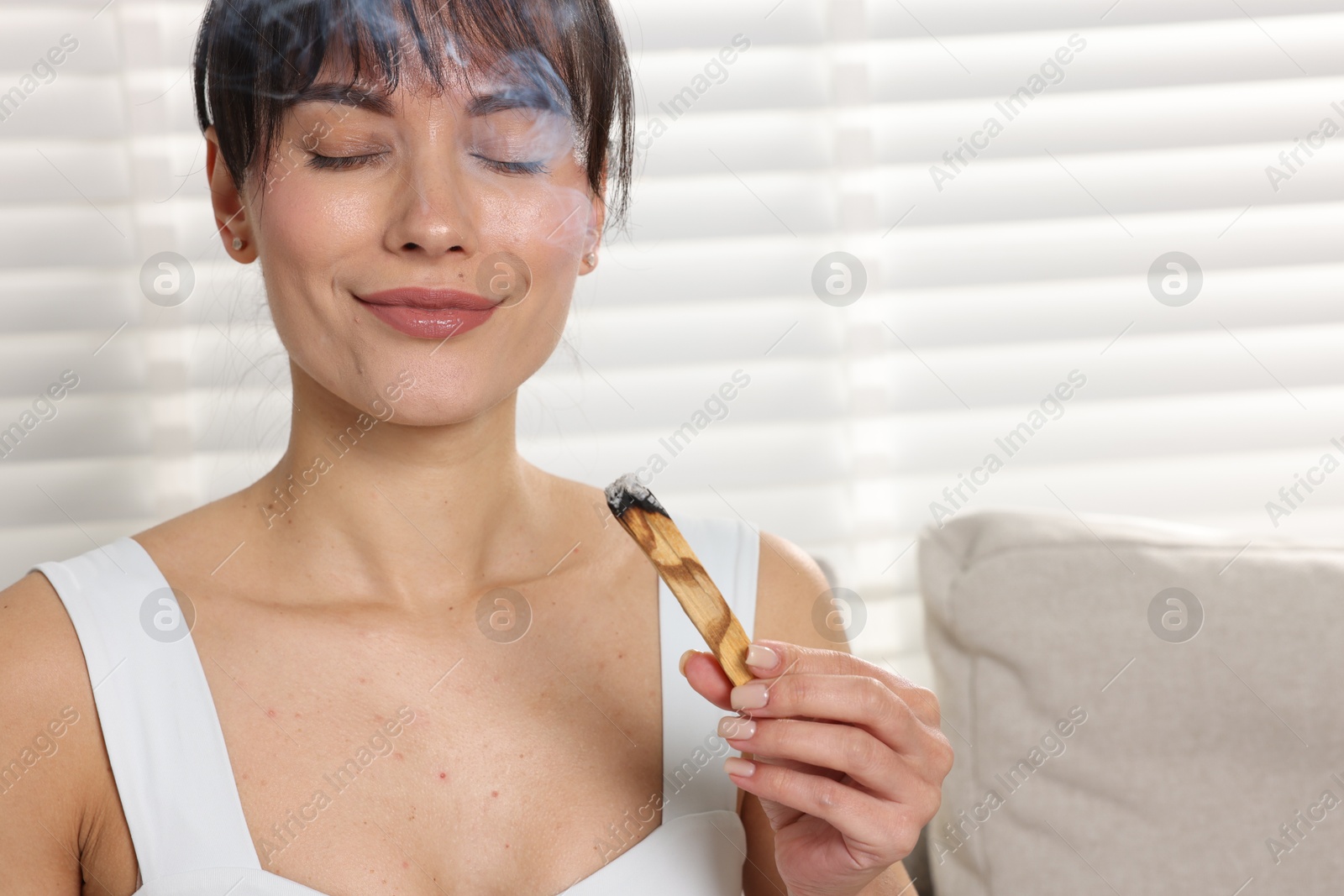 Photo of Woman with smoldering palo santo stick at home, space for text