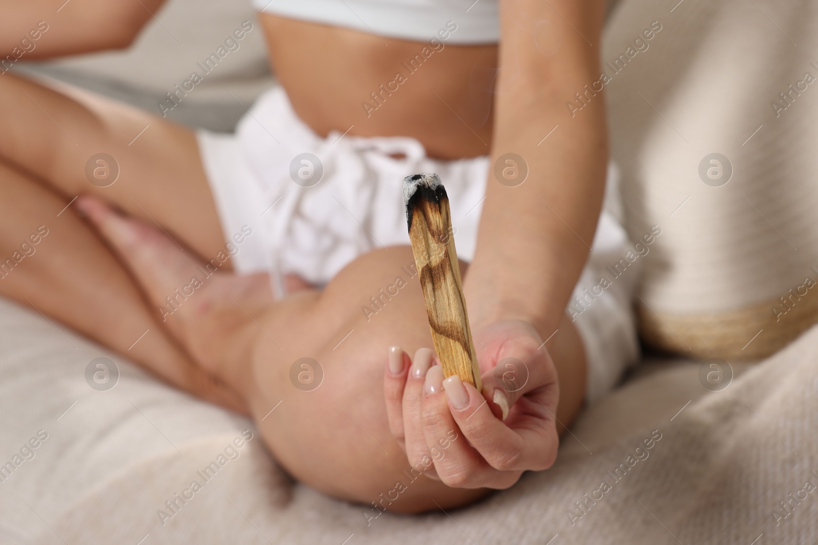 Photo of Woman with smoldering palo santo stick meditating on sofa at home, closeup