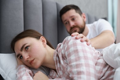 Photo of Man comforting his resentful girlfriend on bed at home, selective focus