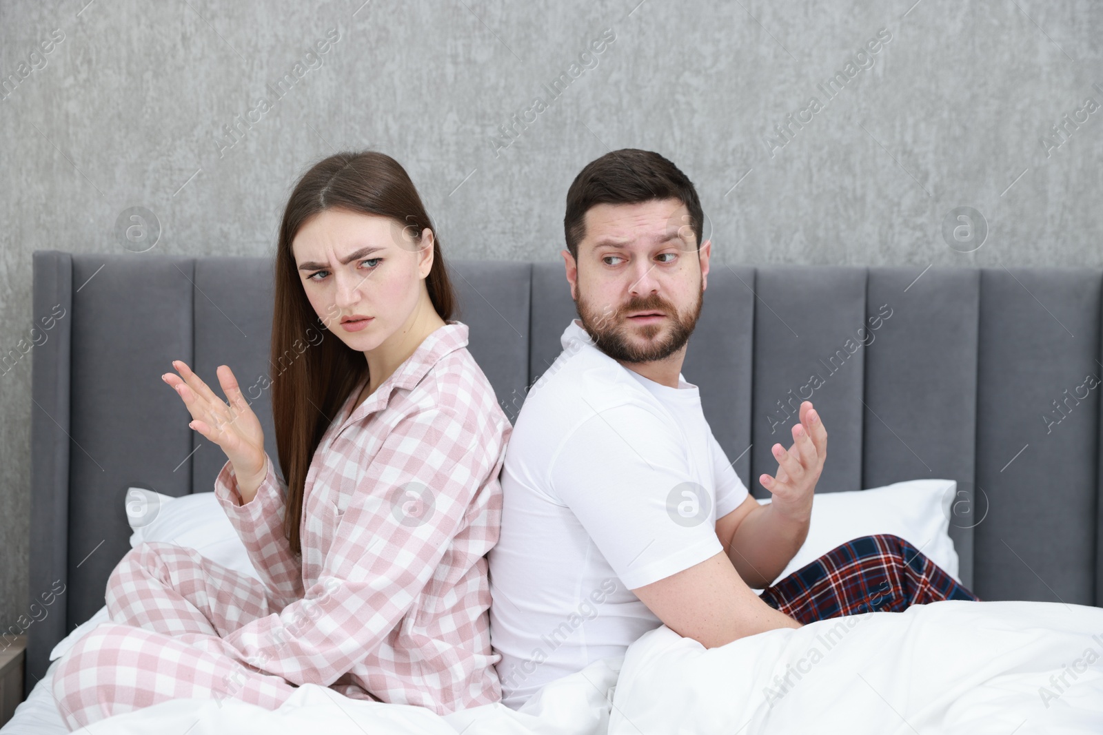 Photo of Resentful couple sitting on bed and arguing at home