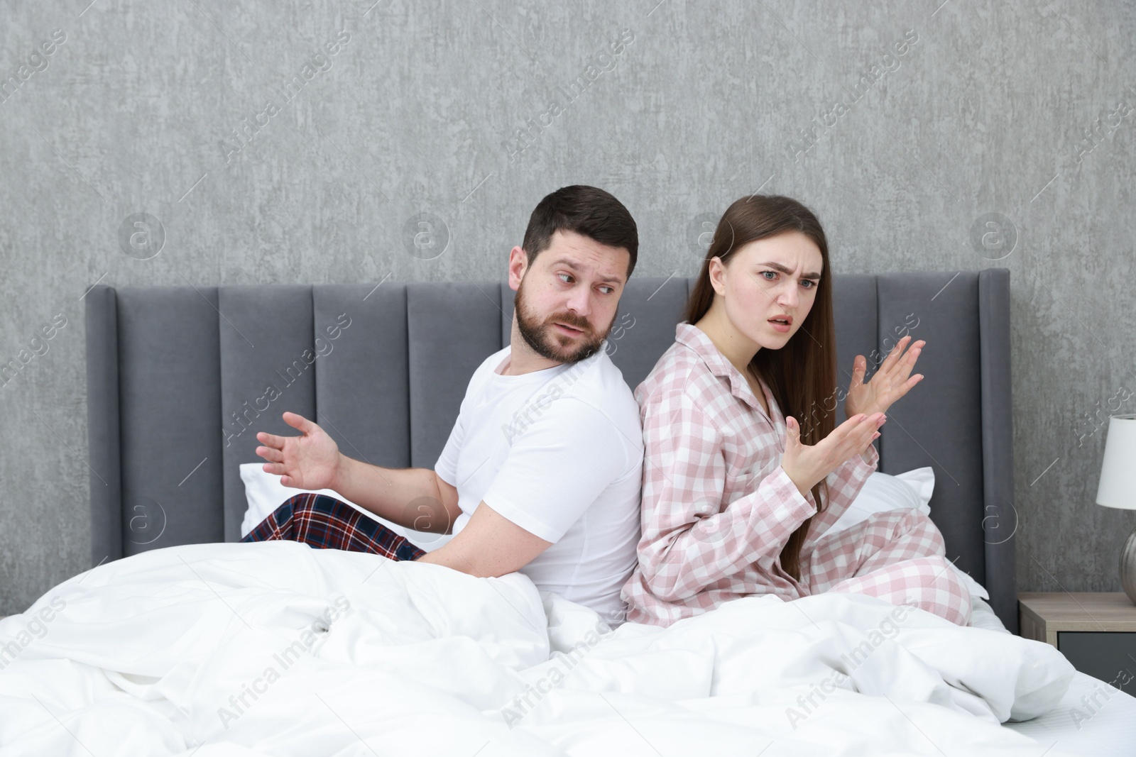 Photo of Resentful couple sitting on bed and arguing at home