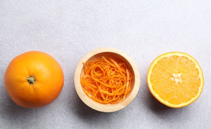 Photo of Fresh orange zest in bowl, whole and cut fruits on grey textured table, flat lay. Space for text