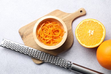 Photo of Fresh orange zest in bowl, whole, cut fruits and grater on grey textured table, flat lay