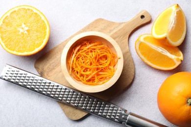 Photo of Fresh orange zest in bowl, whole, cut fruits and grater on grey textured table, flat lay