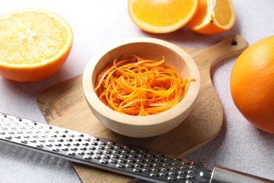 Photo of Fresh orange zest in bowl, fruits and grater on grey textured table, closeup