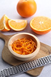 Photo of Fresh orange zest in bowl, fruits and grater on grey textured table, closeup