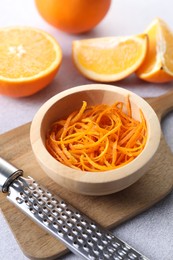 Photo of Fresh orange zest in bowl, fruits and grater on grey textured table, closeup