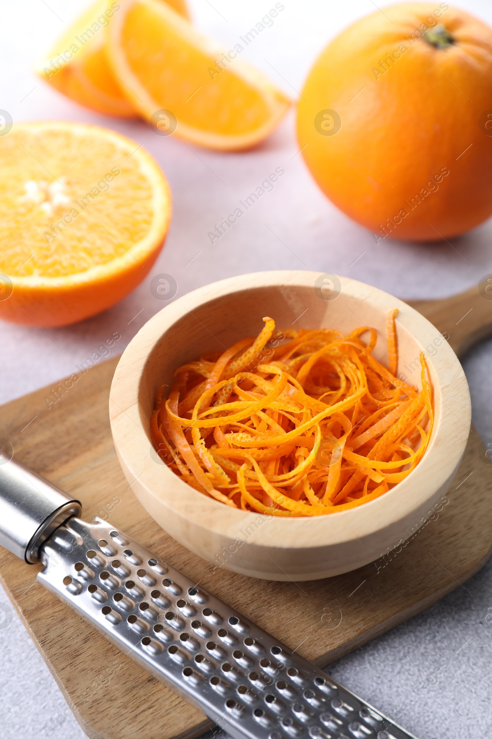 Photo of Fresh orange zest in bowl, fruits and grater on grey textured table, closeup