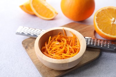 Photo of Fresh orange zest in bowl, fruits and grater on grey textured table, closeup