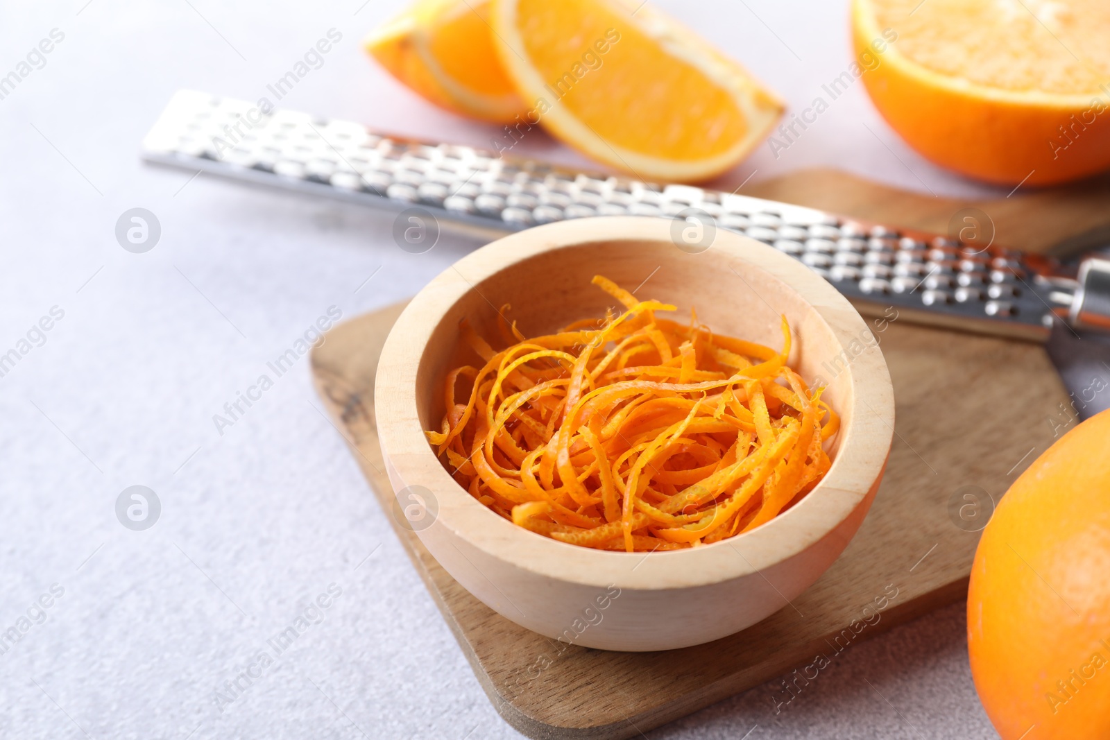 Photo of Fresh orange zest in bowl, fruits and grater on light textured table, closeup