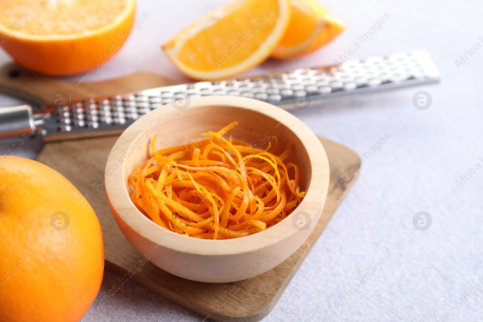 Photo of Fresh orange zest in bowl, fruits and grater on light textured table, closeup