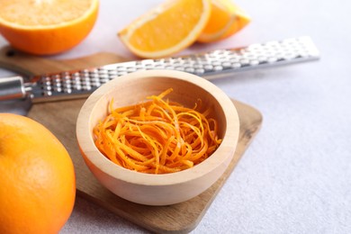 Photo of Fresh orange zest in bowl, fruits and grater on light textured table, closeup