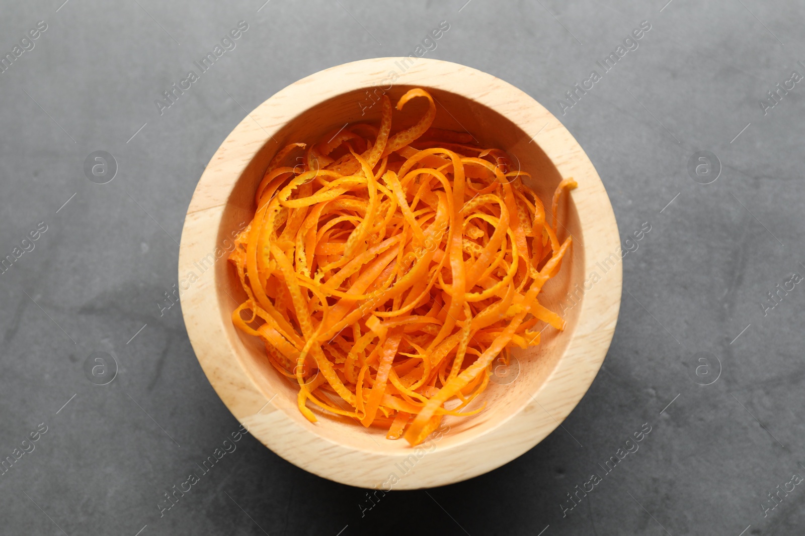 Photo of Fresh orange zest in bowl on grey textured table, top view