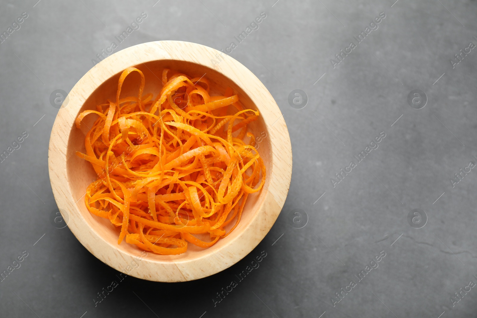 Photo of Fresh orange zest in bowl on grey textured table, top view. Space for text