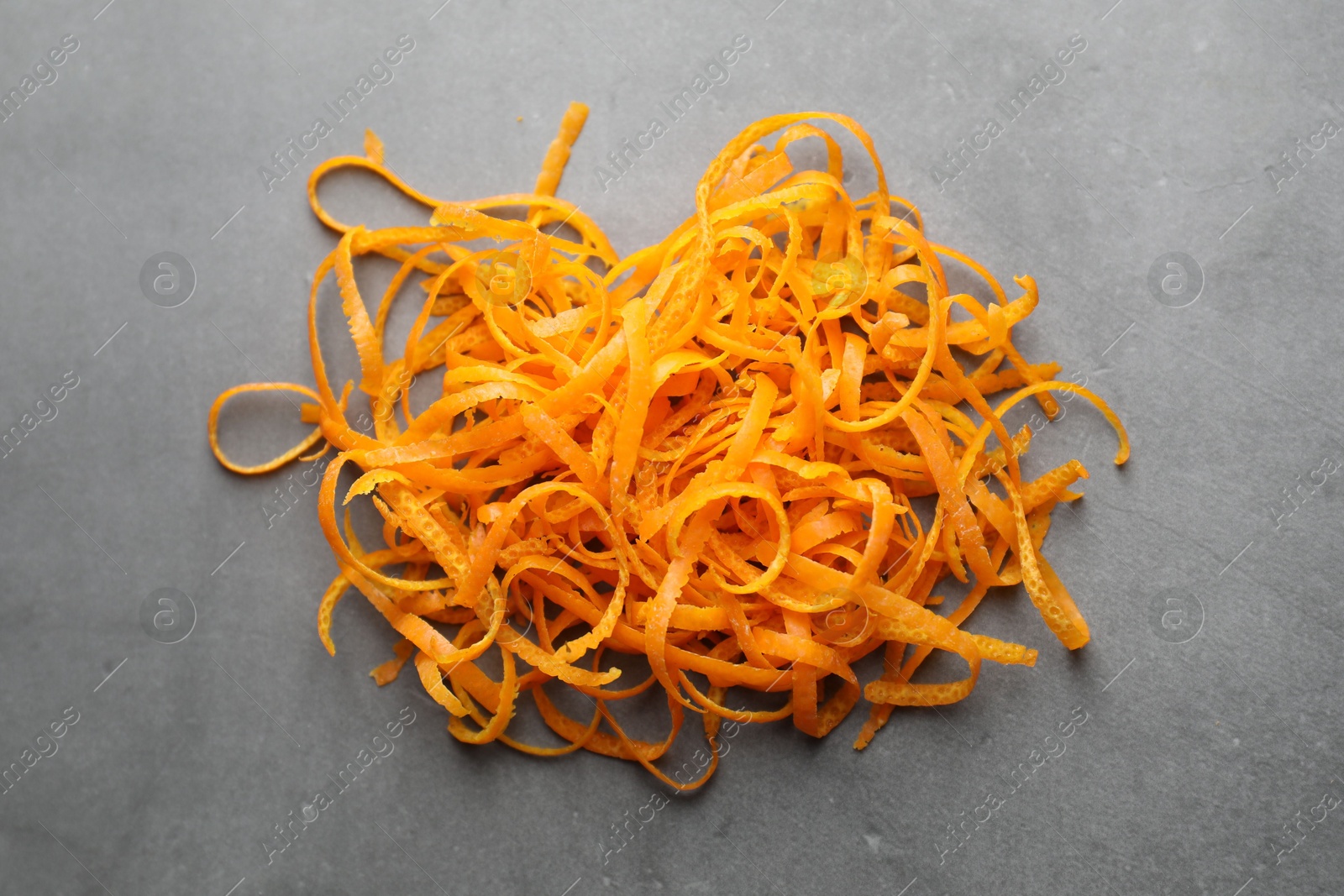 Photo of Pile of fresh orange zest on grey textured table, above view