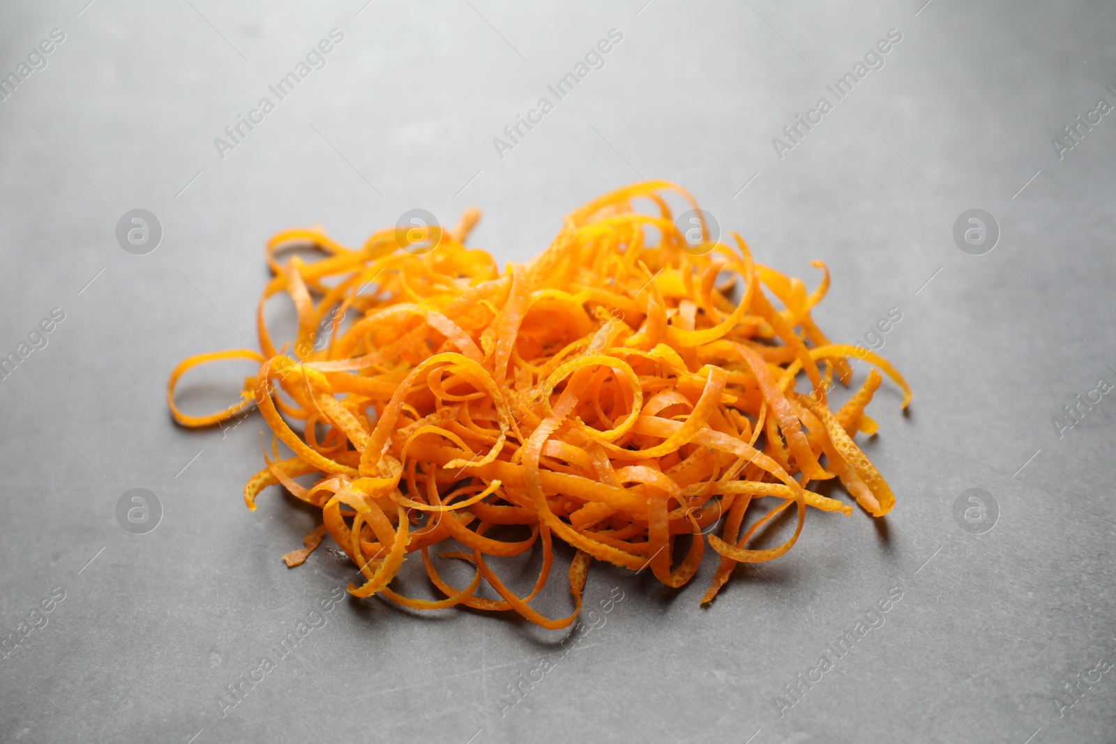 Photo of Pile of fresh orange zest on grey textured table, closeup