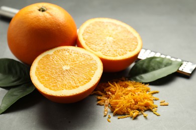 Photo of Pile of fresh orange zest, fruits, grater and leaves on grey table, closeup