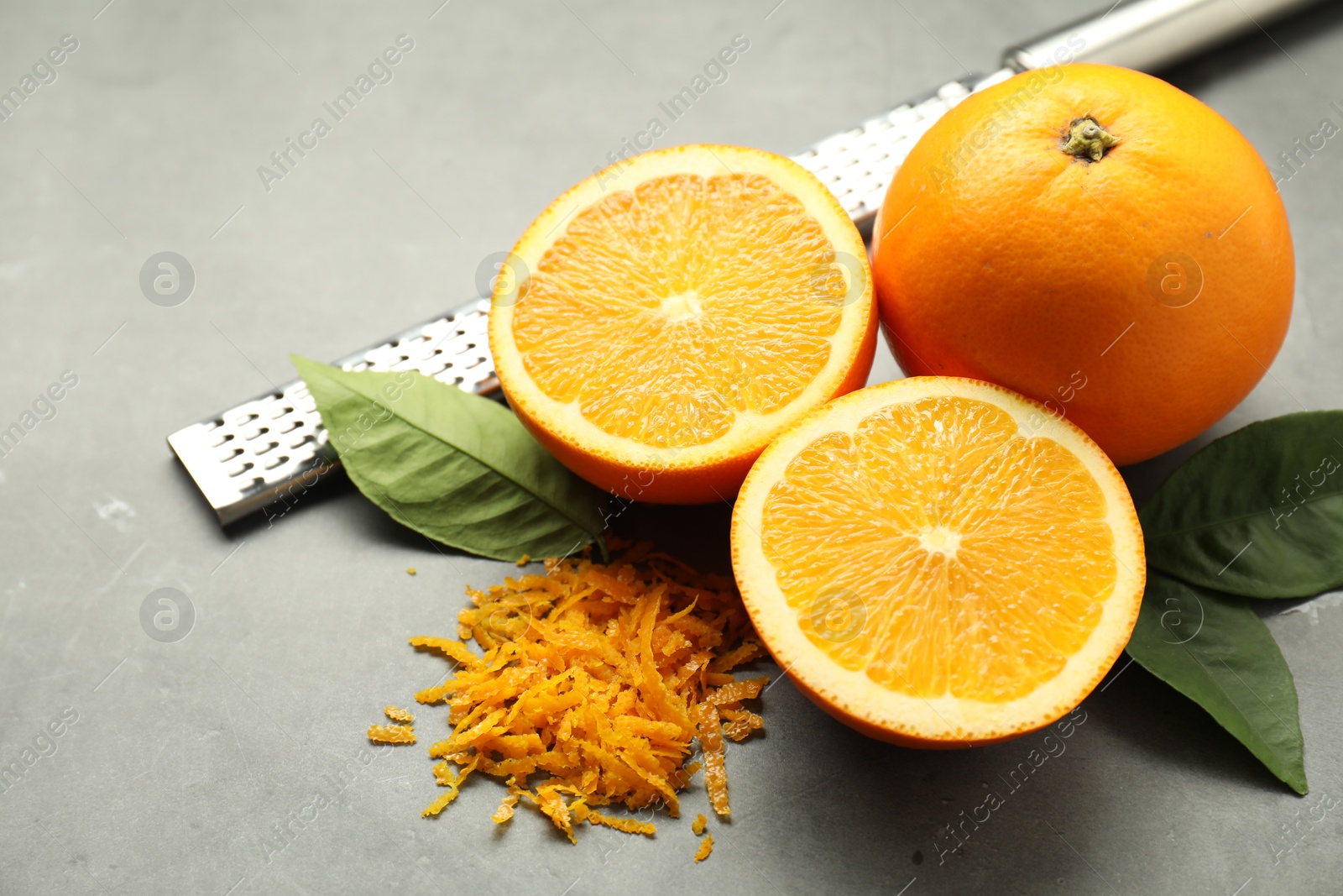 Photo of Pile of fresh orange zest, fruits, grater and leaves on grey table, closeup